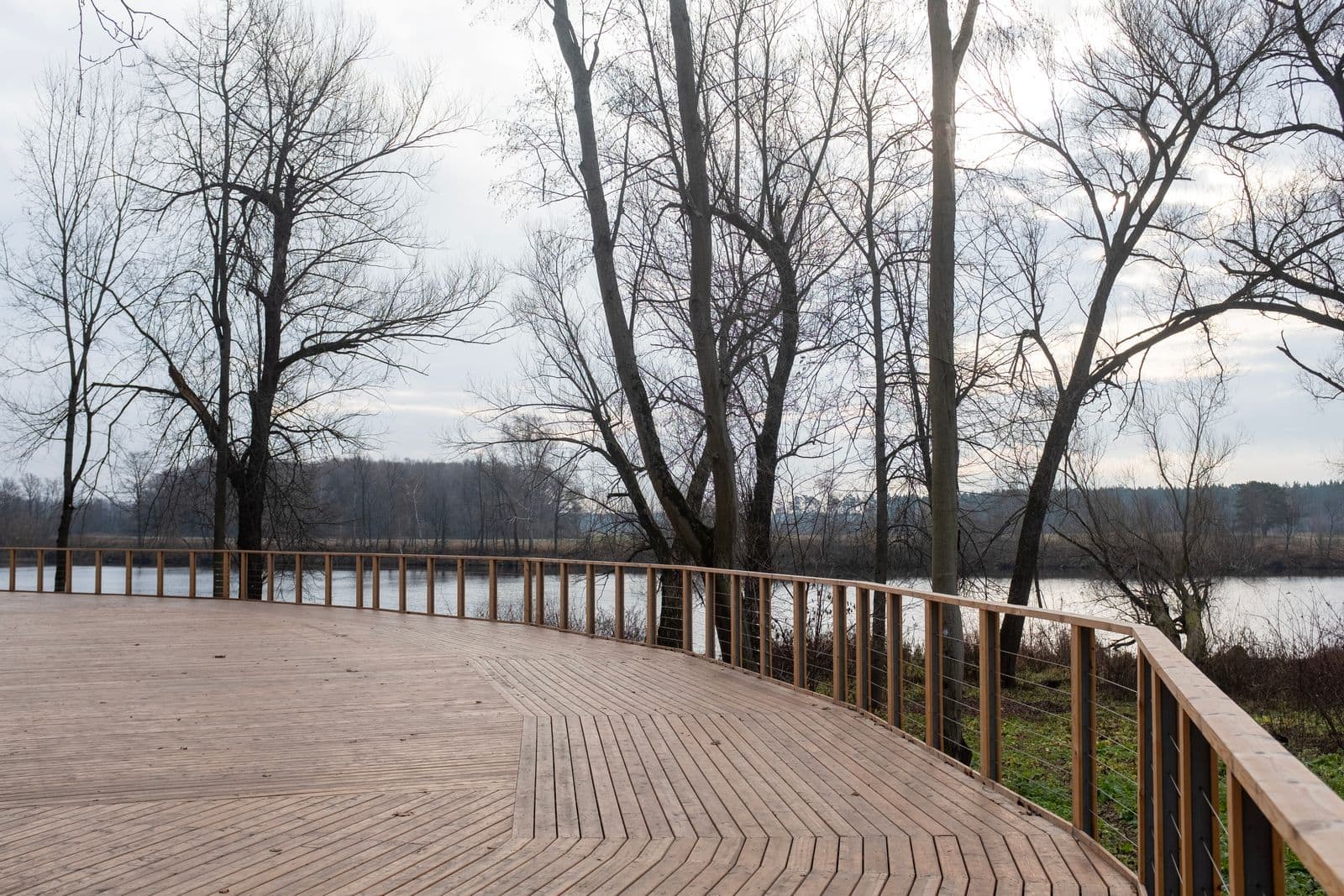 Curved wood deck with a railing above a lake in winter